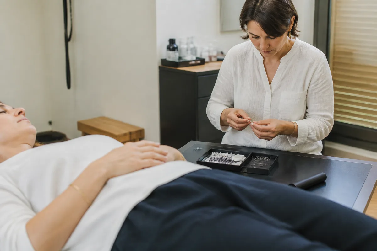 Séance réelle d'acupuncture avec une personne allongée et un praticien préparant les aiguilles dans un cabinet sobre