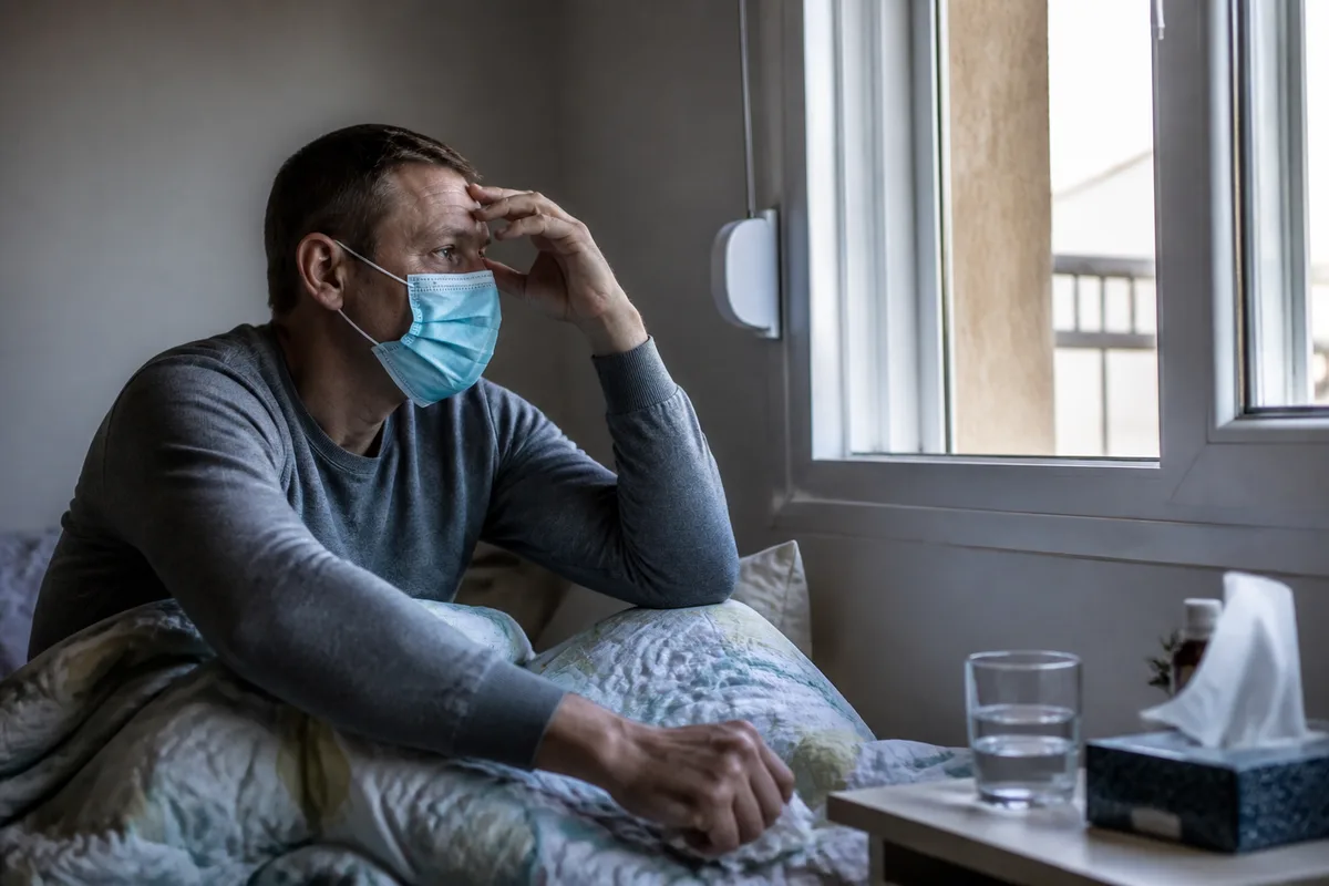 Personne malade à la maison portant un masque près d’une fenêtre ouverte