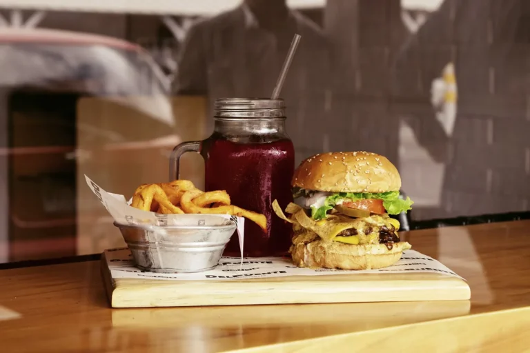 Burger au fromage, frites et boisson rouge servis sur une planche en bois