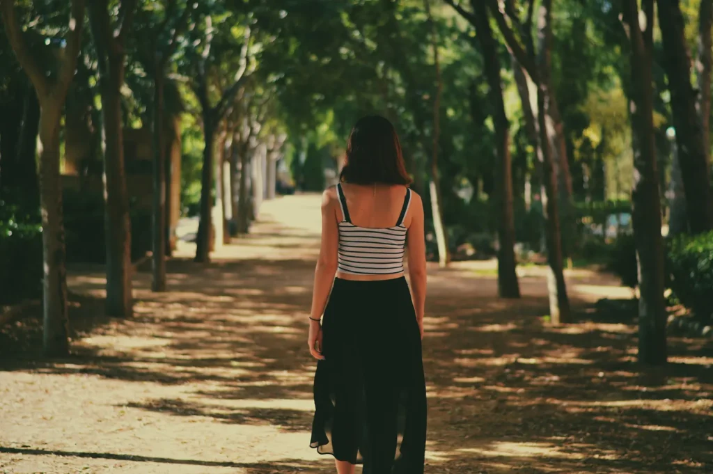 Femme marchant de dos dans une allée ombragée bordée d'arbres