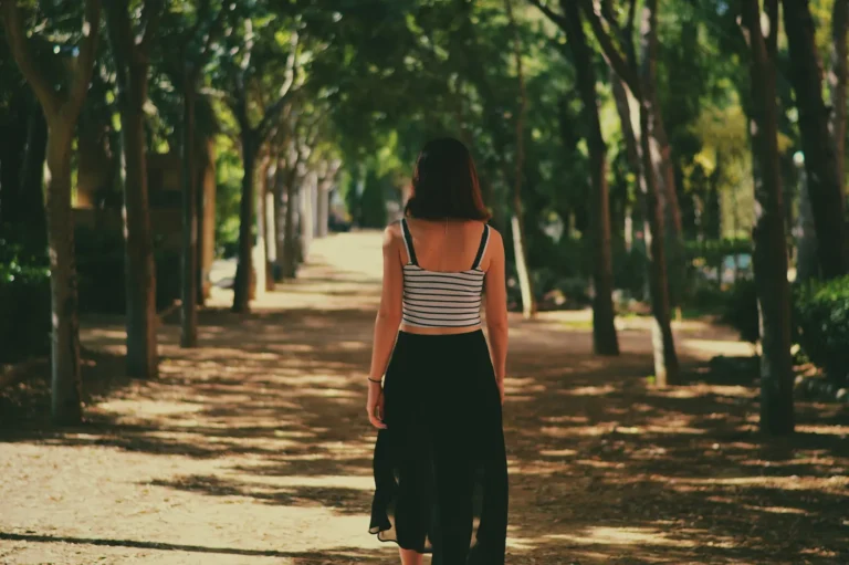 Femme marchant de dos dans une allée ombragée bordée d'arbres